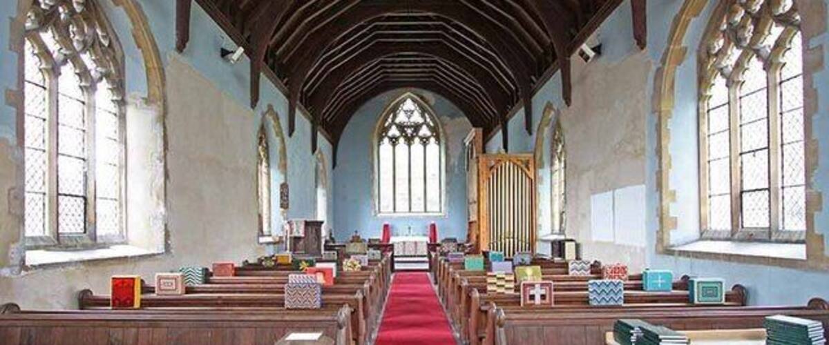 A church interior with wooden pews, a red carpet, and tall stained glass windows.