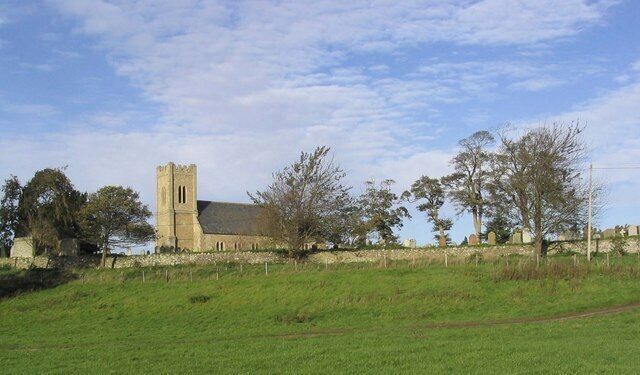 A church with a tall tower and a stone building, surrounded by trees and a grassy field.