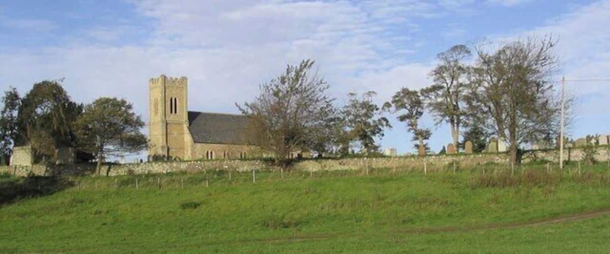 A church with a tall tower and a stone building, surrounded by trees and a grassy field.