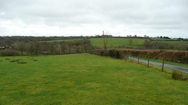 A rural landscape with a grassy field, a road, and rolling hills in the background.