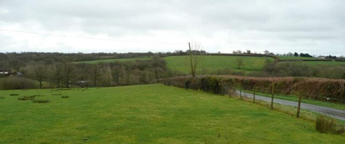 A rural landscape with a grassy field, a road, and rolling hills in the background.