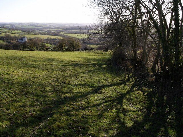 Field above Aller Cross Filleigh Footpath 15 drops down the side of this field, commanding views across the line of the A361 link road and the valley of the Nadrid Water. The shadows are cast by trees not just on the boundary of this field, but by those on a field boundary running off to the right. The building on the left, Snurridge, is in SS7028.