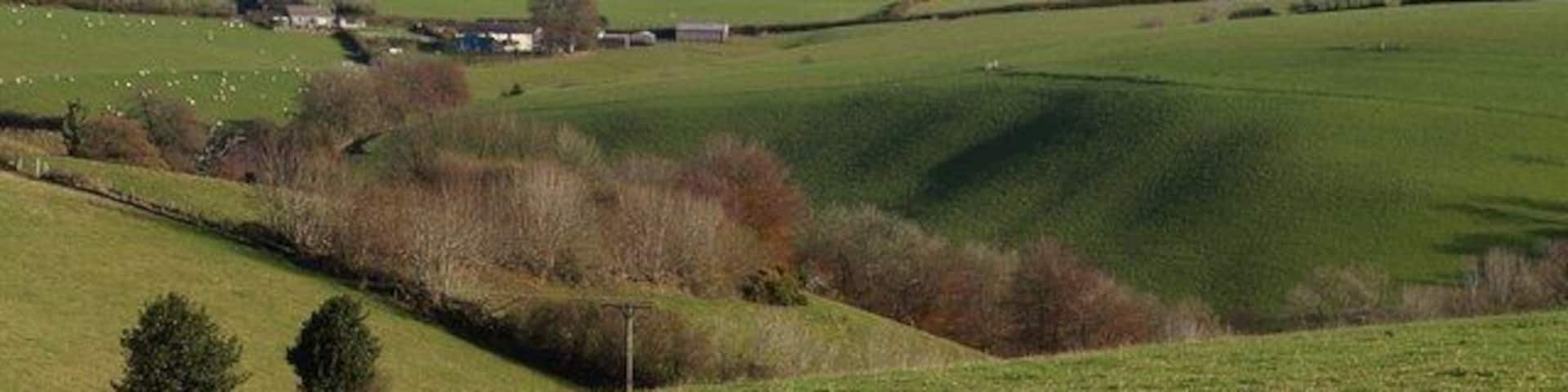 Rolling green hills, a small cluster of buildings, and distant mountains.
