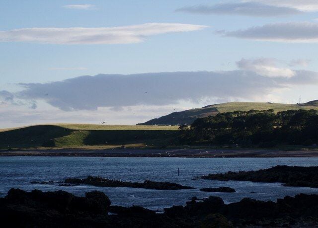 Across Inverbervie Bay to Hallgreen Castle The wave cut platform of the northern end of the bay is in shadow in the foreground. The setting sun catches the raised beach at Hallgreen Castle on the southern side of the bay.