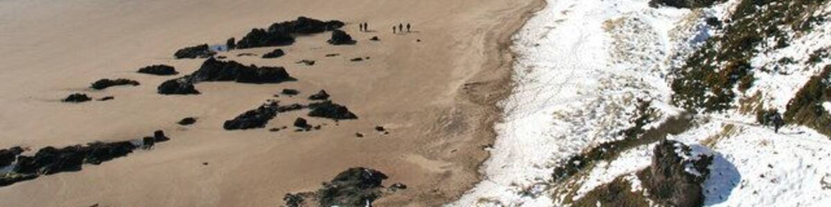 Une plage enneigée, parsemée d’affleurements rocheux, sous un ciel dégagé.