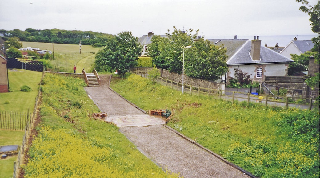 Site of former Johnshaven station, 2002. View eastward from New Road bridge, towards Inverbervie: ex-NBR Montrose - Inverbervie branch. The station was probably behind me: it and the line (parallel to Back Road) were closed to passengers 1/10/51, to goods not until 23/5/66. The track-bed seems to have been restored for recreational purposes.
