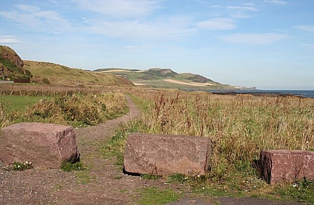 A rural landscape with a dirt path, large rocks, and rolling hills in the distance.