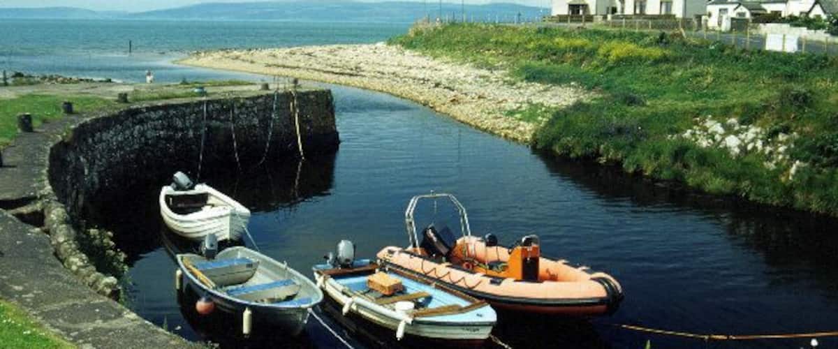 A narrow waterway with boats docked on the left, a lock on the right, and houses in the background.