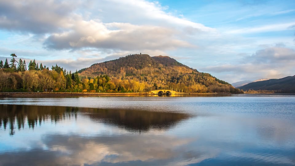 A calm lake with a mountain in the background and a bridge in the middle.