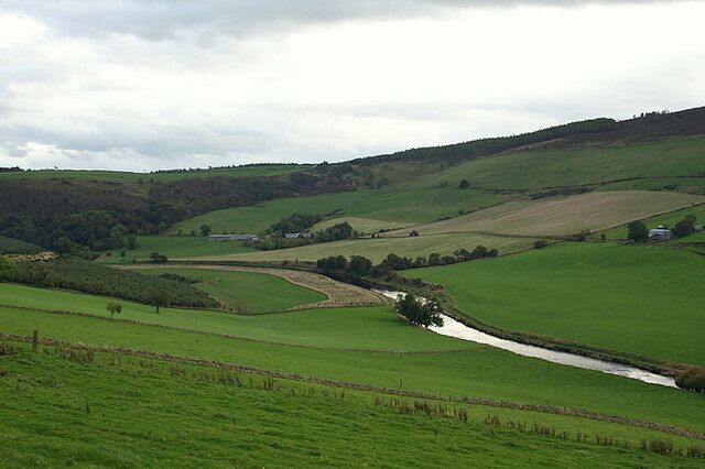Rolling green hills, a small stream, and a distant farmhouse.