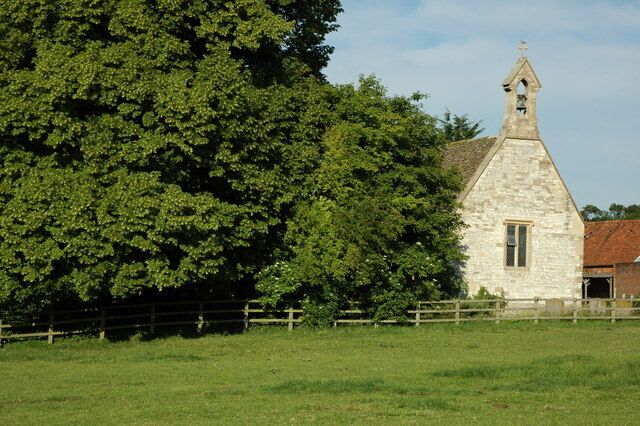 A stone church with a bell tower, surrounded by a grassy field and a large tree.