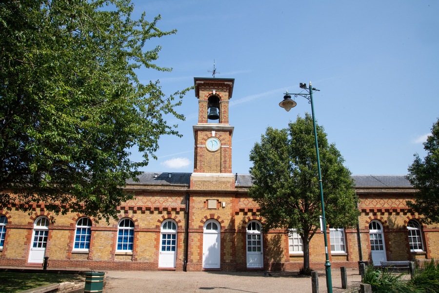 A historic brick building with a clock tower, arched windows, and a bell.