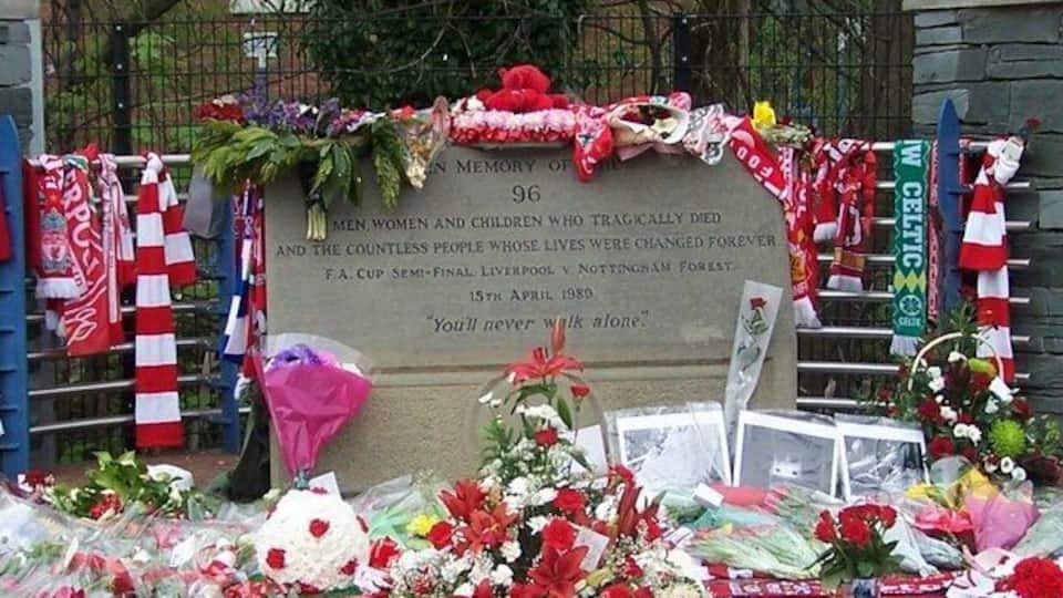 A memorial with a plaque, flowers, and flags.