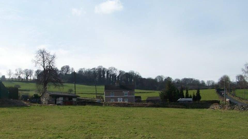 A rural landscape with open fields, a few houses, and a road.