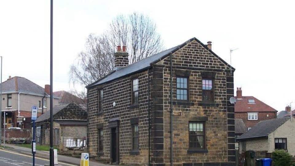 A stone building with a pitched roof, a street lamp, and a blue trash bin.