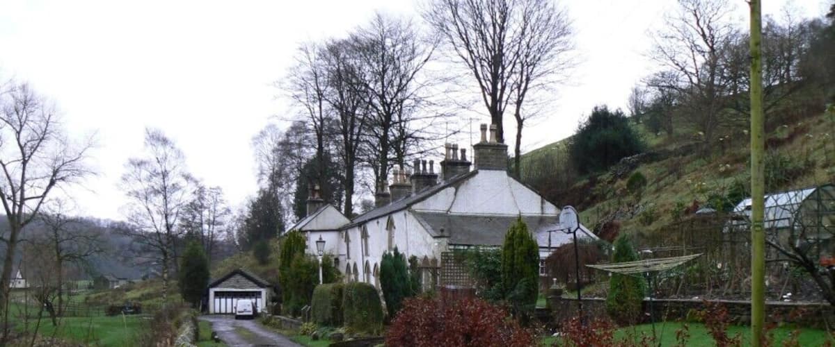 A rural road leading to a white house with a thatched roof, surrounded by trees and a small pond.
