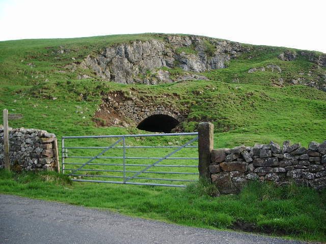 Un portón de piedra y la entrada de un túnel en un paisaje cubierto de hierba.