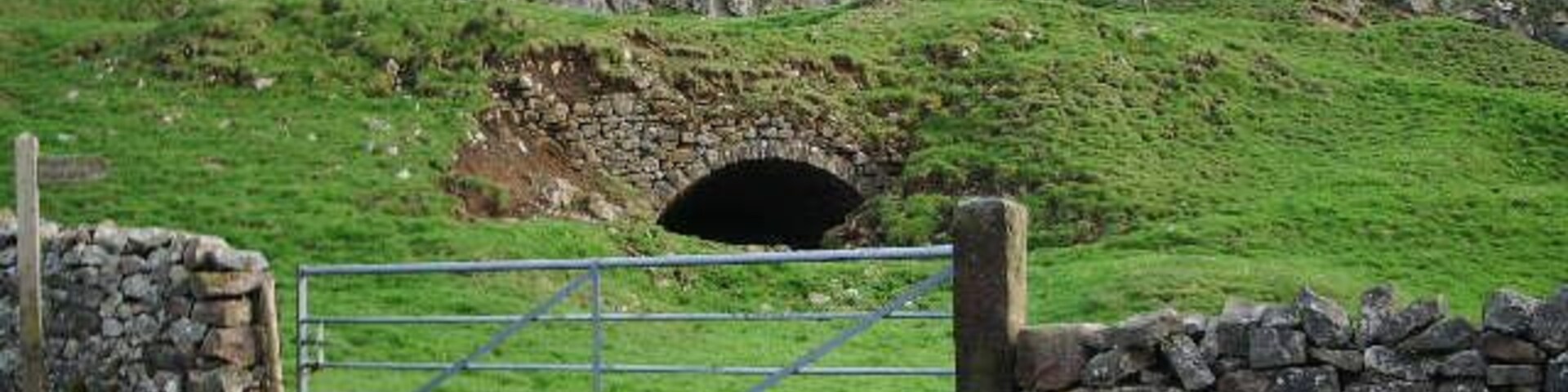 Un portón de piedra y la entrada de un túnel en un paisaje cubierto de hierba.