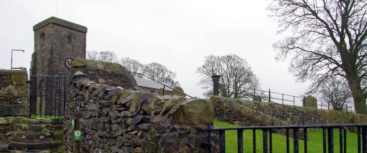 A stone wall with a clock tower, a metal fence, and a grassy area.