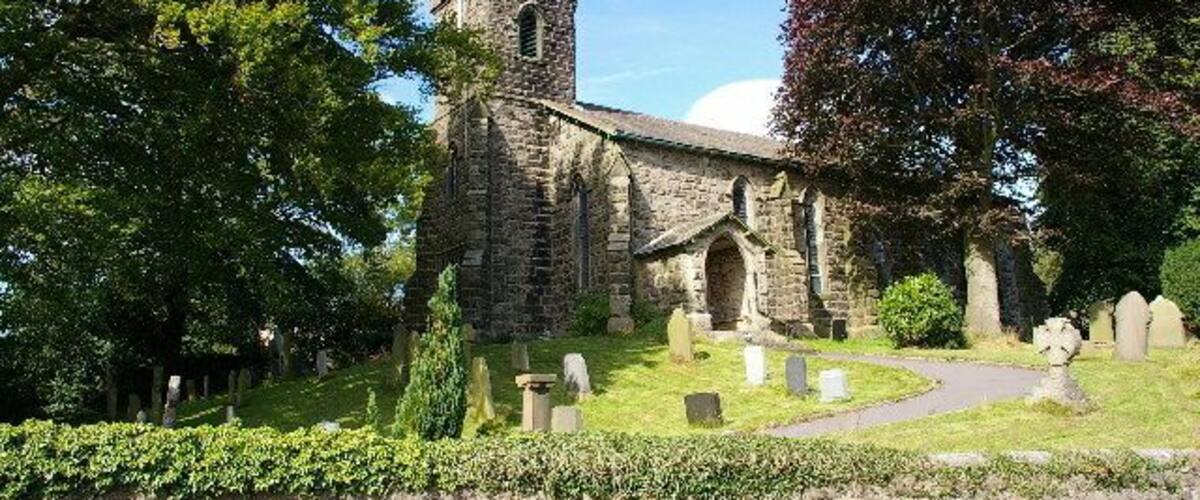 A stone church with a bell tower, surrounded by trees and a cemetery.