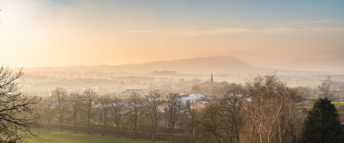 A misty landscape with a prominent hill, scattered houses, and leafless trees.