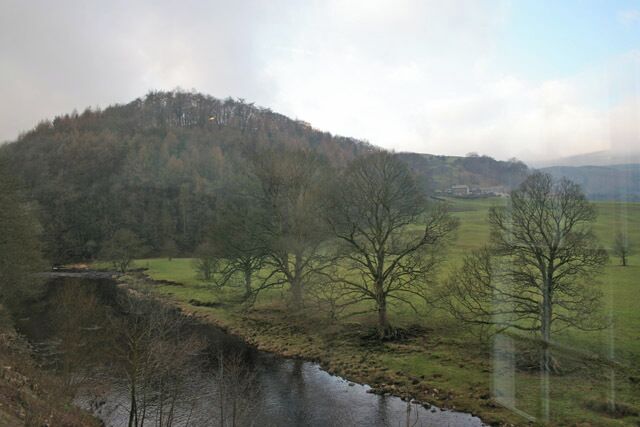 A river flowing through a valley with a forested hill in the background.