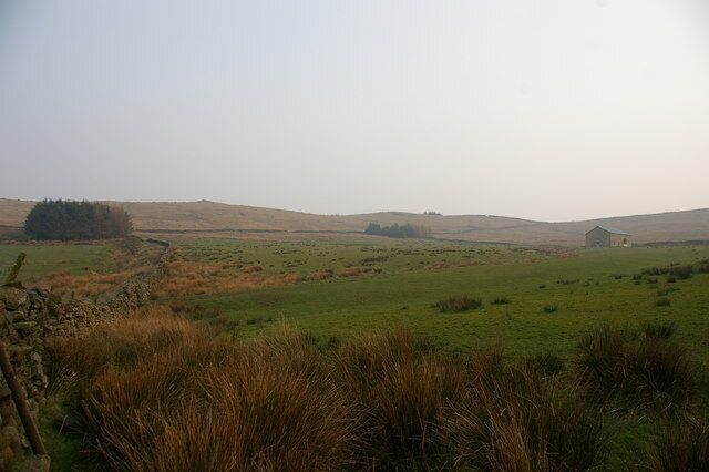 A rural landscape with rolling hills, a stone wall, and a small building in the distance.