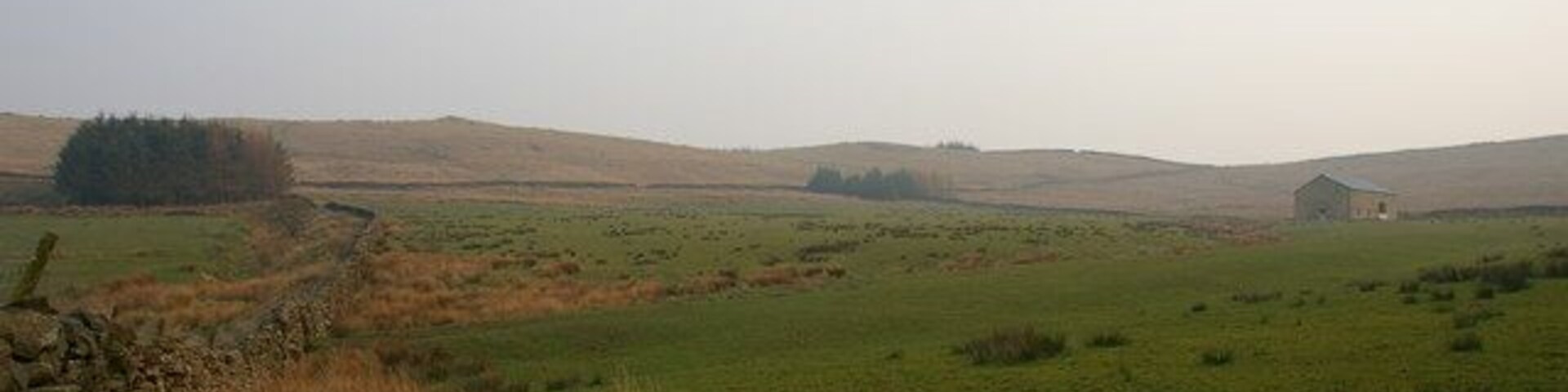 A rural landscape with rolling hills, a stone wall, and a small building in the distance.