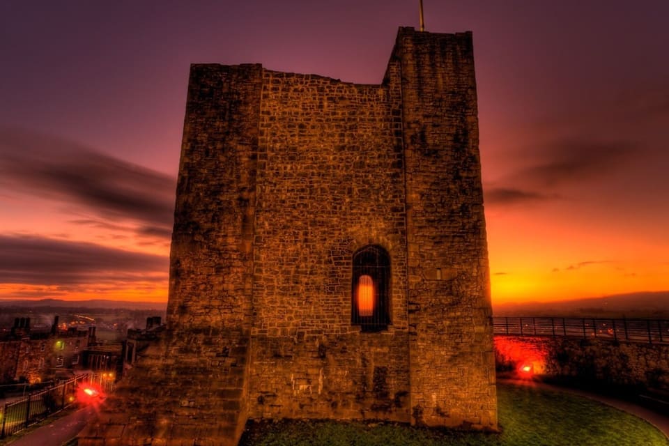 A medieval stone tower with a flag, surrounded by a grassy area and a cityscape in the background.