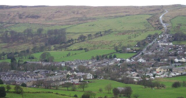 A rural village nestled in a valley with rolling green hills in the background.