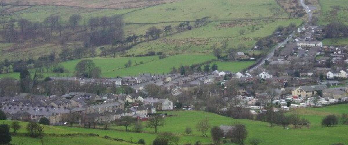 A rural village nestled in a valley with rolling green hills in the background.