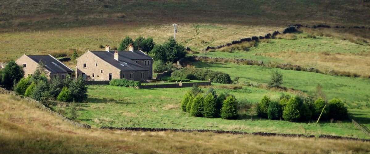 Un paysage rural avec deux maisons en pierre, un mur de pierre et une colline en arrière-plan.