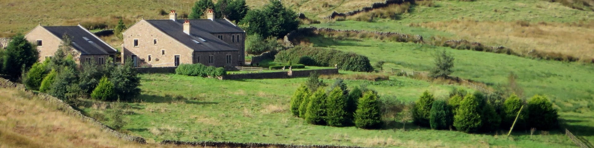 A rural landscape with two stone houses, a stone wall, and a hill in the background.