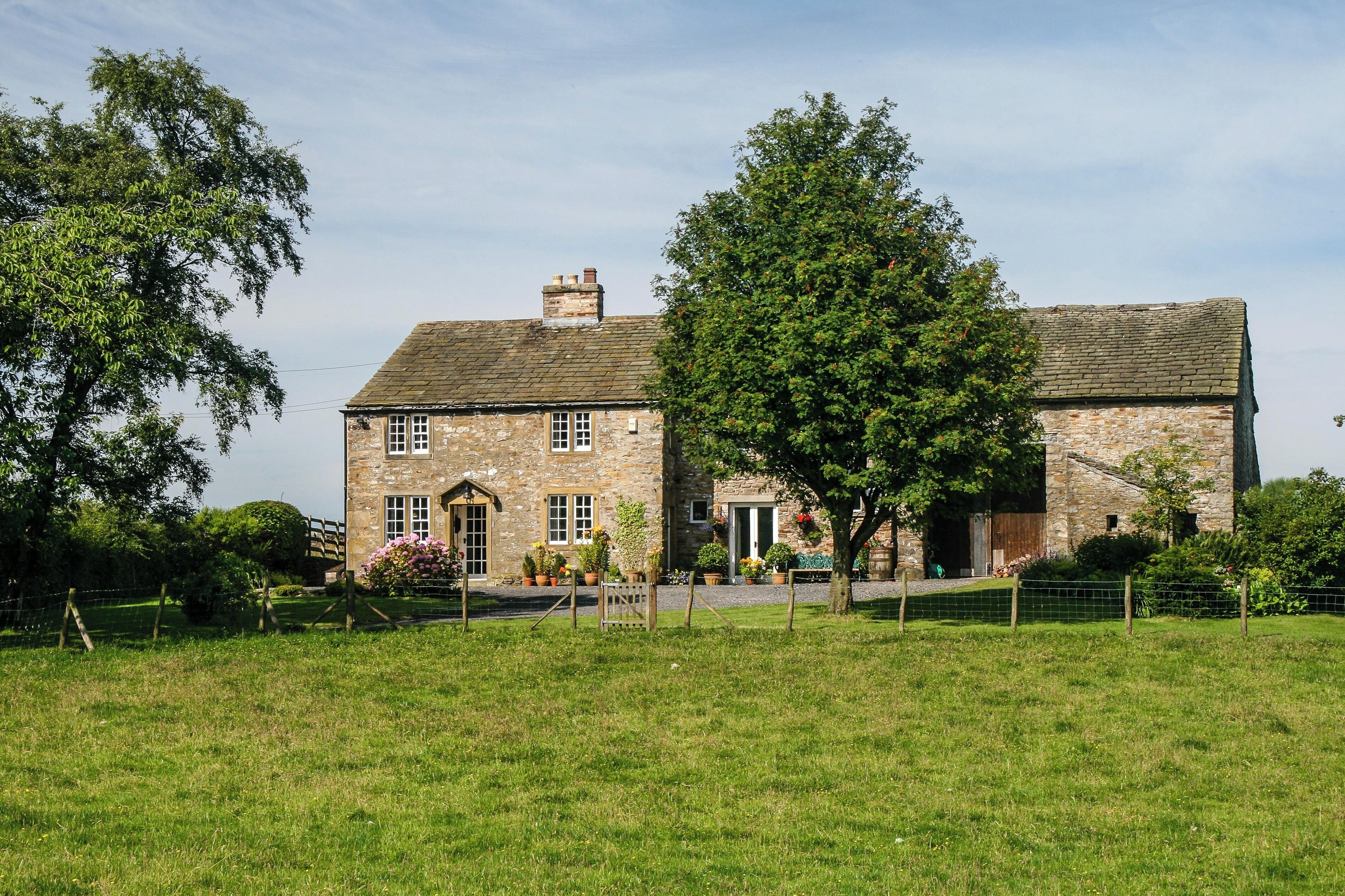 A stone house with a brick roof, surrounded by a grassy field and trees.
