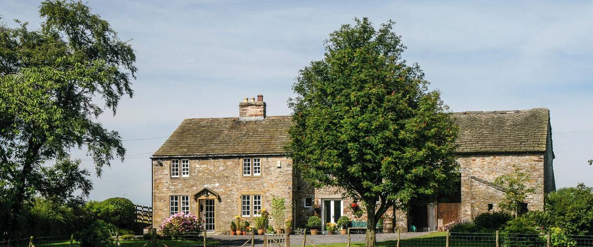 A stone house with a brick roof, surrounded by a grassy field and trees.
