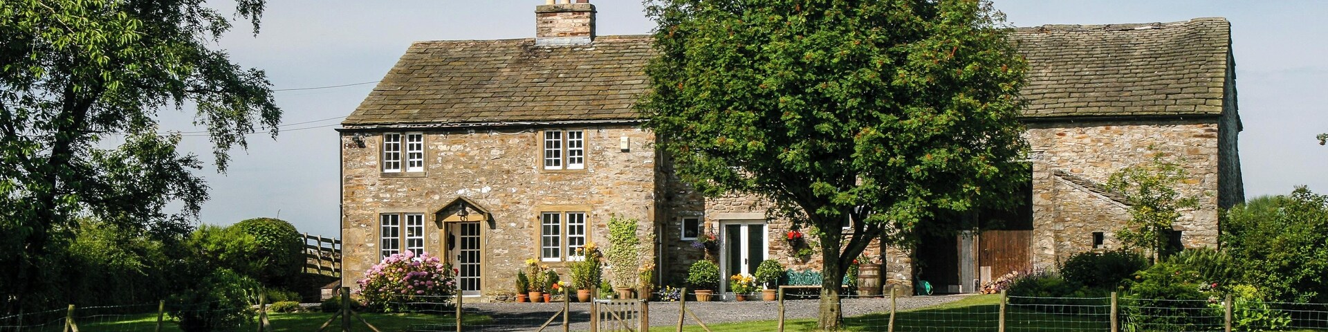 A stone house with a brick roof, surrounded by a grassy field and trees.