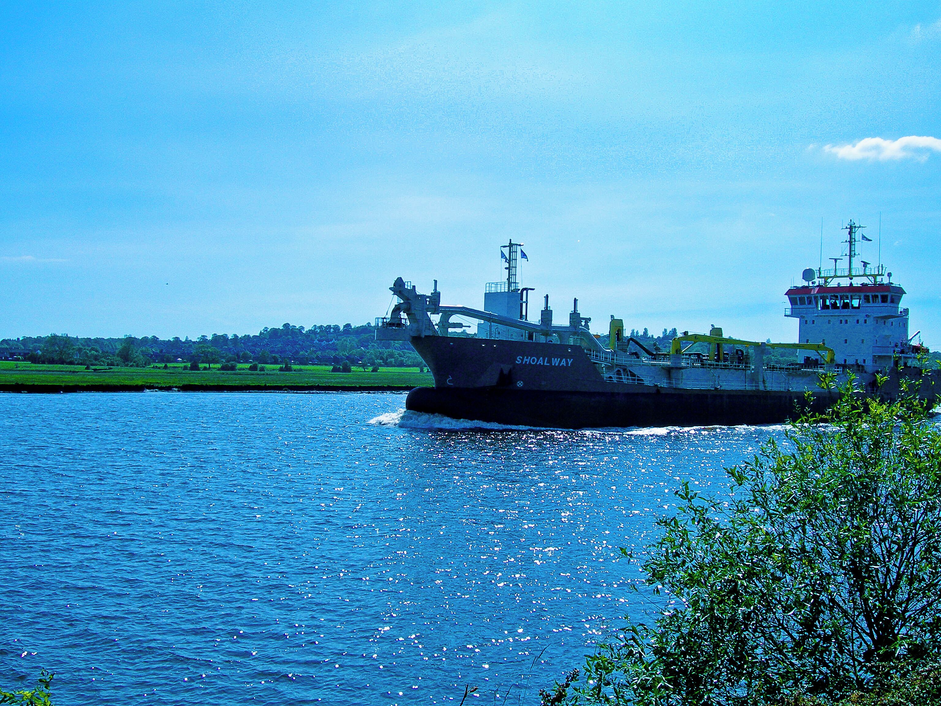 A large cargo ship named "Shoal Way" on a river.