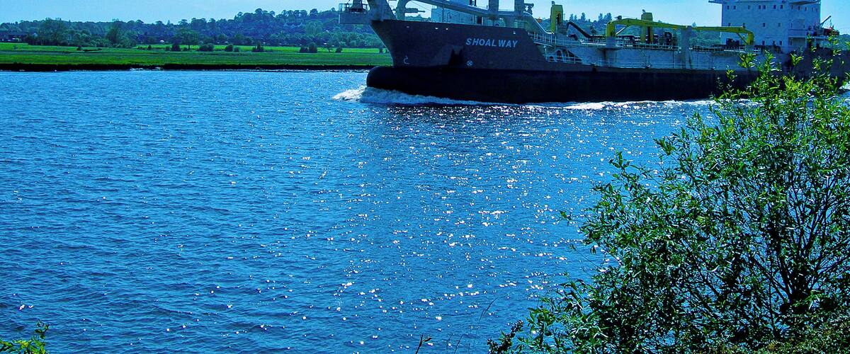 A large cargo ship named "Shoal Way" on a river.