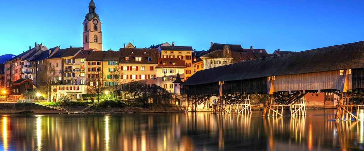 A calm river reflecting buildings, a prominent clock tower, and traditional architecture.