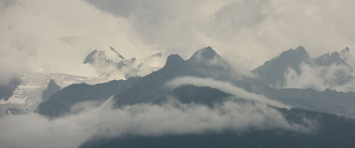 A mountain range with snow-capped peaks and clouds.