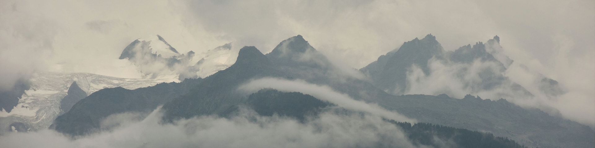 A mountain range with snow-capped peaks and clouds.