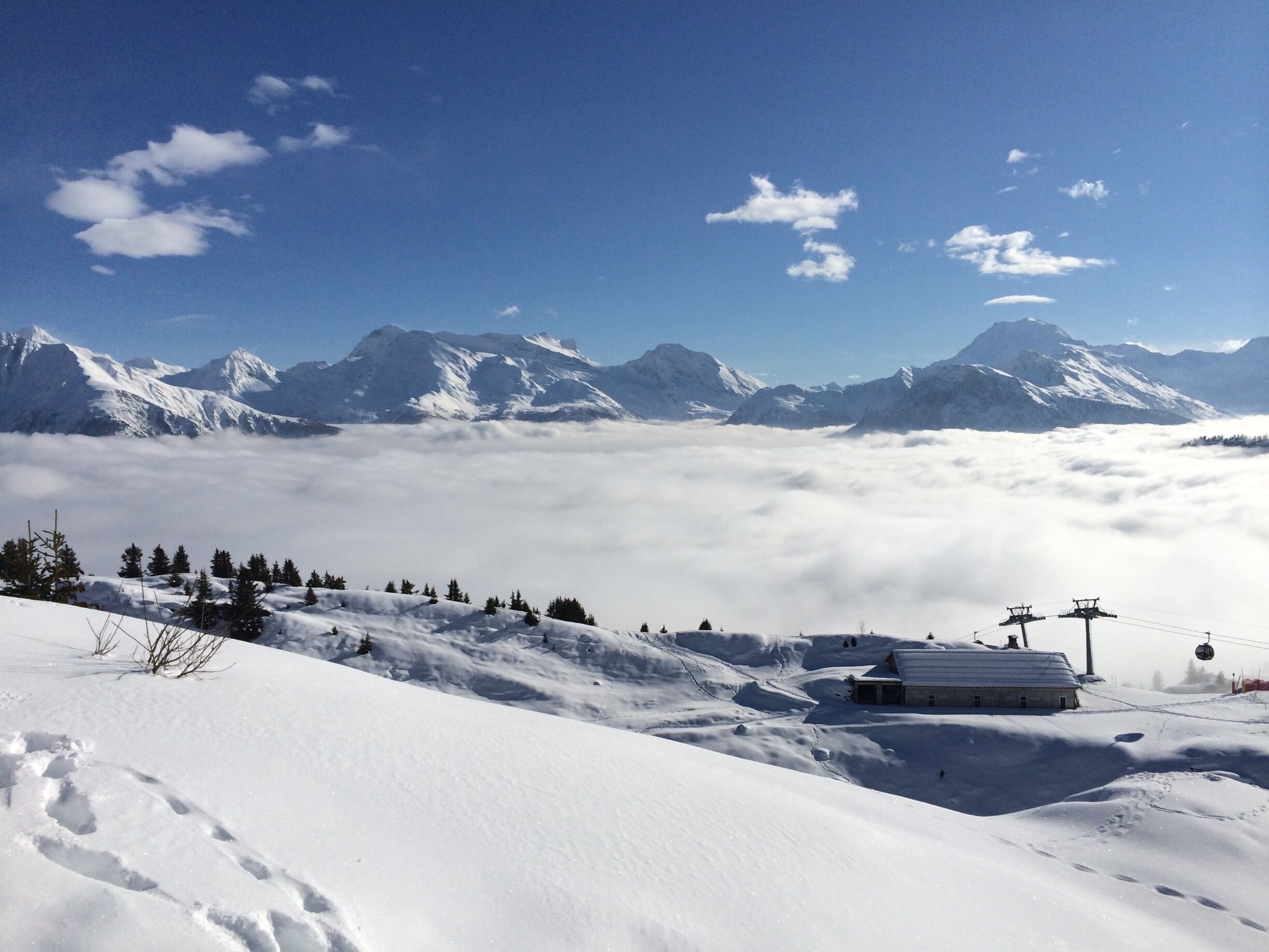 A snow-covered mountain landscape with a ski lift, a cabin, and a clear sky.