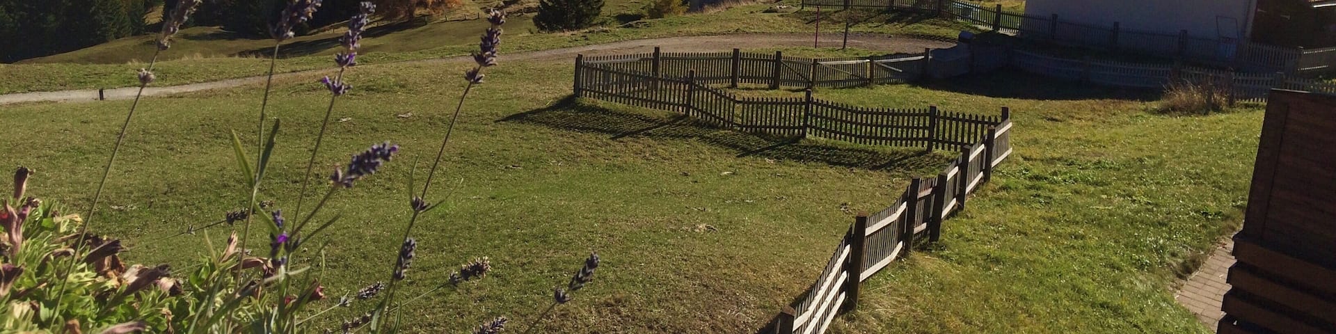A mountainous landscape with snow-capped peaks, a wooden fence, and a small building.
