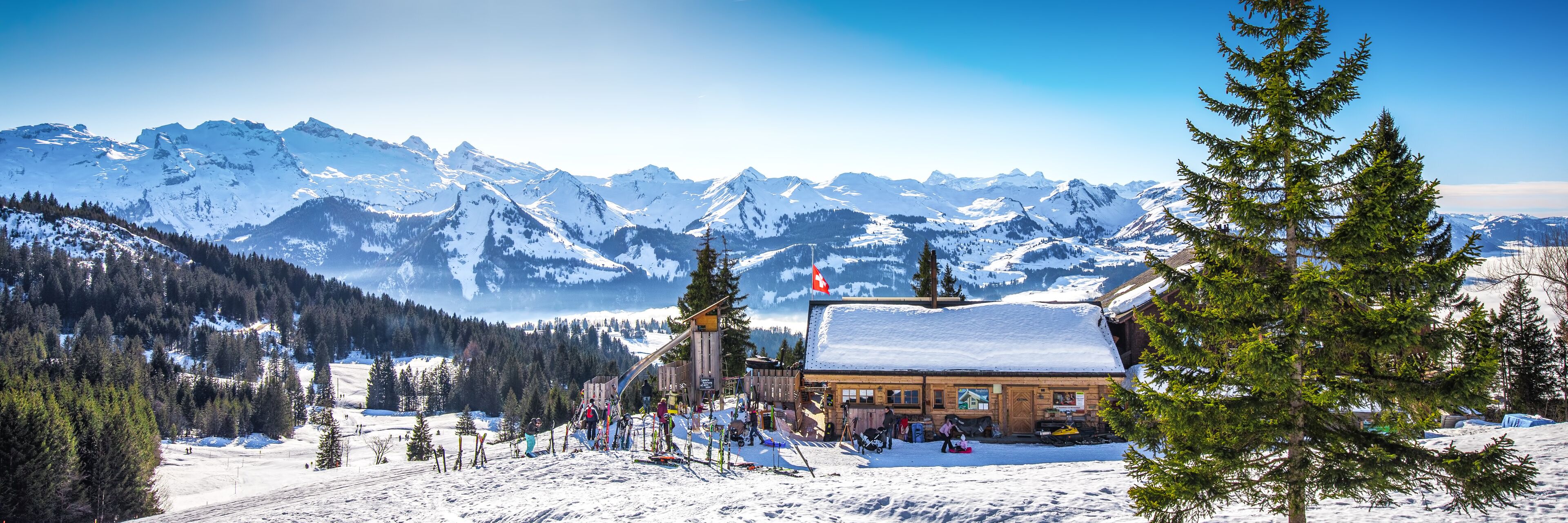 A ski resort with a lodge, snow-covered mountains, and pine trees.