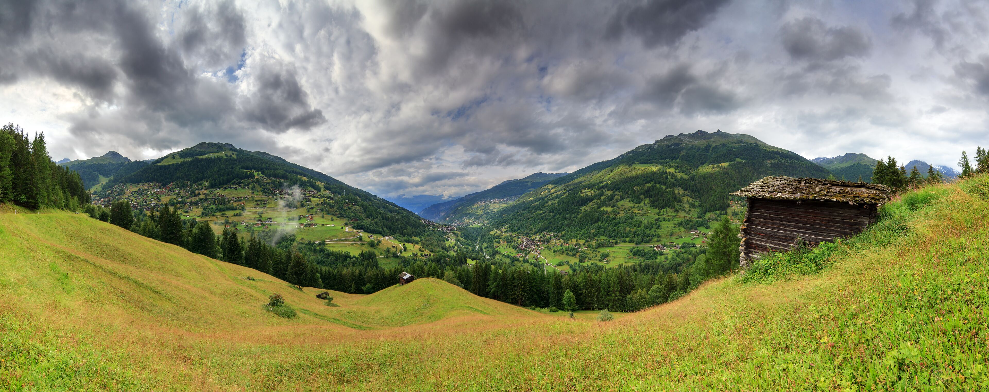 A mountainous landscape with a village nestled in the valley, surrounded by lush greenery and a thatched-roof hut.
