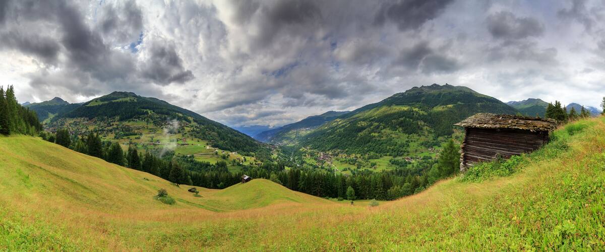 A mountainous landscape with a village nestled in the valley, surrounded by lush greenery and a thatched-roof hut.