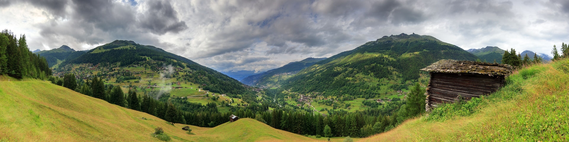 A mountainous landscape with a village nestled in the valley, surrounded by lush greenery and a thatched-roof hut.