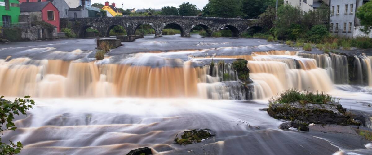 A multi-tiered waterfall with a stone bridge in the background.