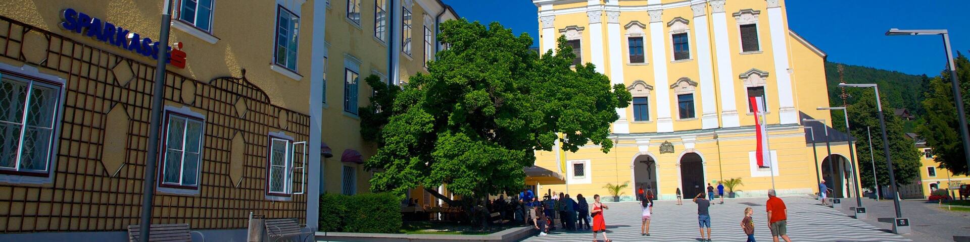 A historic church with two towers, a plaza with people, and a building with a sign.