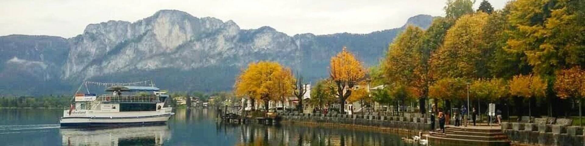 A calm lake with a boat, autumn-colored trees, and mountains in the background.